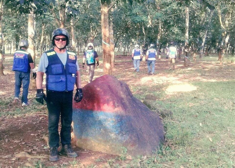 A person standing next to a large rock with a colorful pattern, surrounded by trees in a forested area. 2