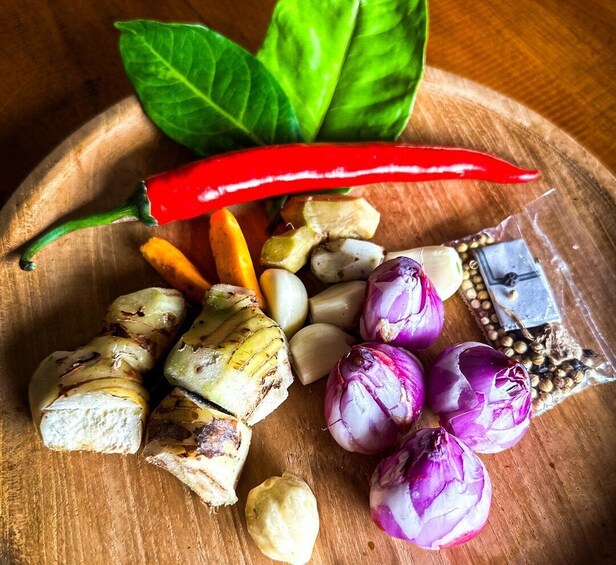 A wooden cutting board with various vegetables and spices, including red chili, carrots, garlic, ginger, onions, and a package of seeds. 3