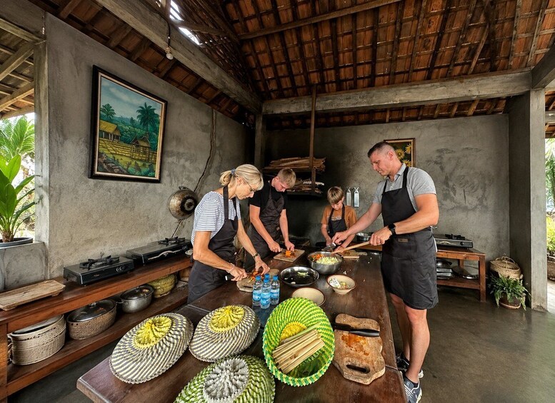 A rustic kitchen with people preparing food, a painting on the wall, and traditional woven baskets. 1