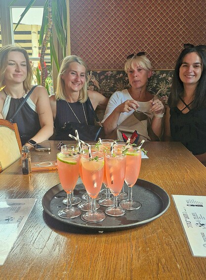 A group of people seated at a table with a tray of pink cocktails garnished with lime and herbs. 2