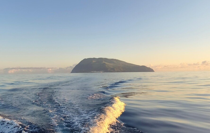 A calm sea with a boat creating a wake, a distant island, and a clear sky. 2