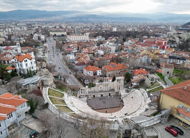 An aerial view of a city with a large, historic amphitheater surrounded by residential buildings and a busy road. 4
