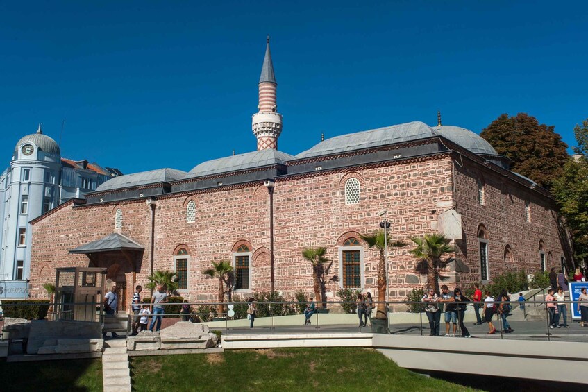A historic mosque with a tall minaret and a dome, surrounded by a small park with palm trees and people. 3