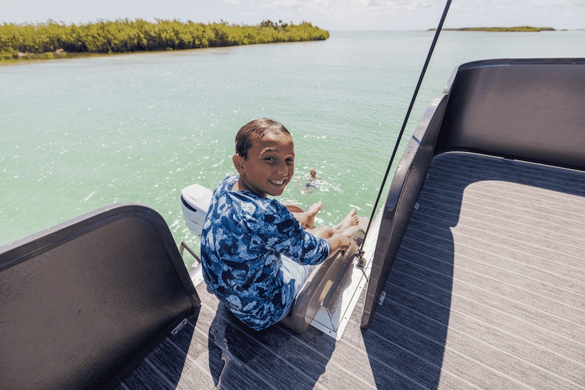 A person sitting on a boat's deck, steering, with calm waters and a distant shoreline in the background. 3