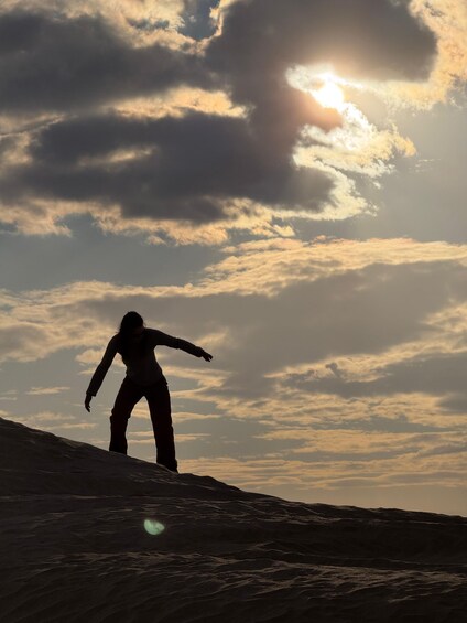 A silhouette of a person snowboarding on a slope with a cloudy sky and the sun setting in the background. 4