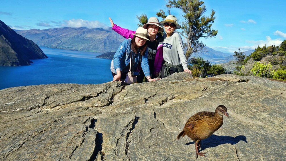 A group of people on a rocky outcrop with a lake and mountains in the background. 1