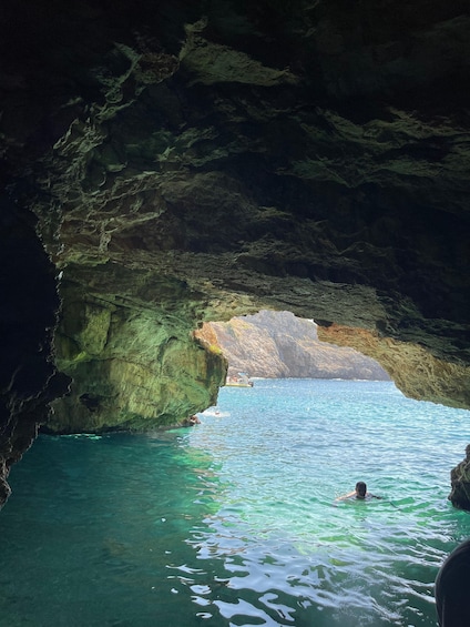 A cave opening to a clear blue sea with a swimmer in the water. 4