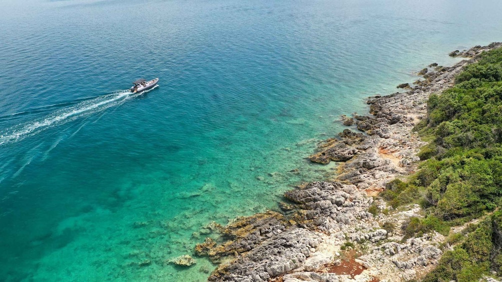 A boat on clear turquoise waters near rocky coastline. 1