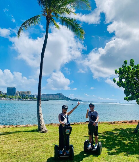 Two people on Segways near a body of water with a palm tree and a cityscape in the background. 5