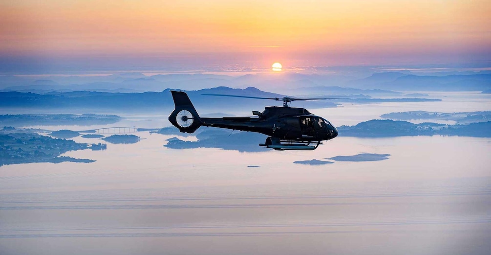 A helicopter flying over a calm body of water during sunset. 1