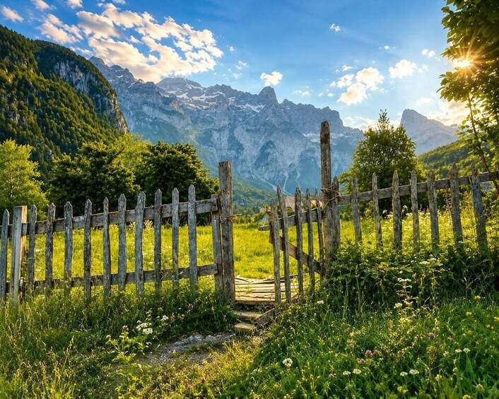 A wooden fence in a lush green meadow with a mountain range in the background. 2