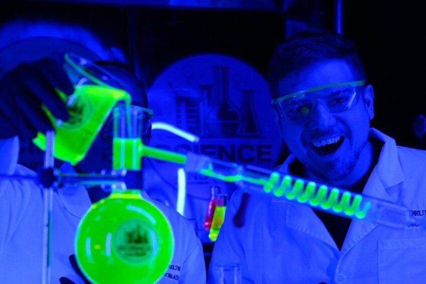 A person in a lab coat conducting a chemistry experiment with a glowing green liquid in a flask. 1