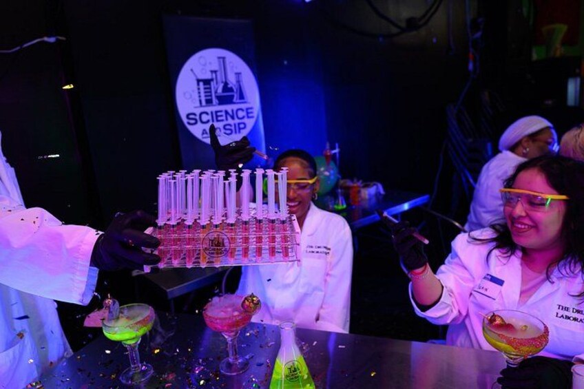 A science-themed event with people in lab coats, a display of test tubes, and a banner reading 'SCIENCE ASIP'. 3