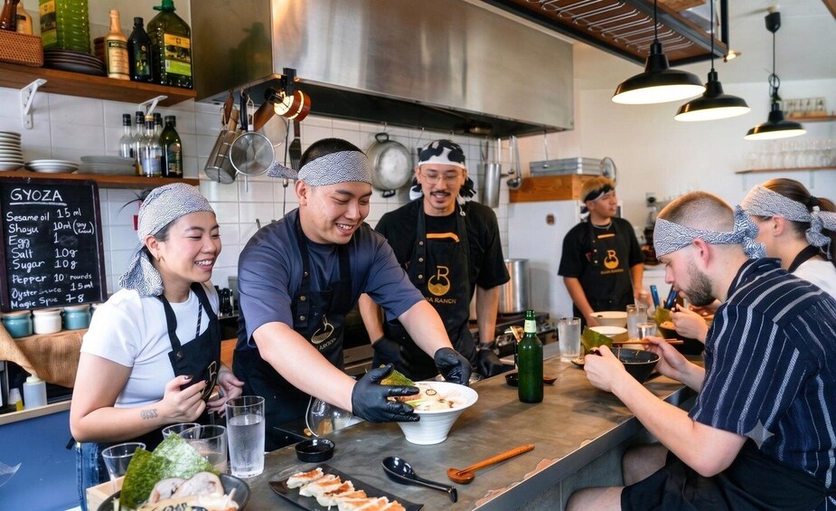 A group of people in a kitchen preparing food, with a menu board visible. 1