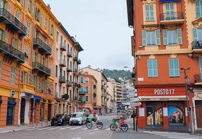 A street with colorful buildings, a Posto17 pharmacy, and a cyclist crossing. 5