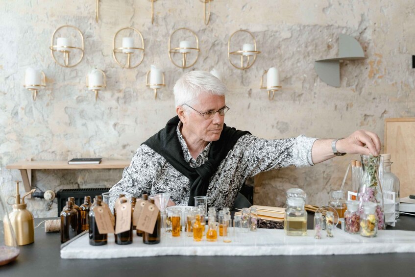 An elderly person arranging bottles on a table in a room with a marble wall and wall-mounted lamps. 4