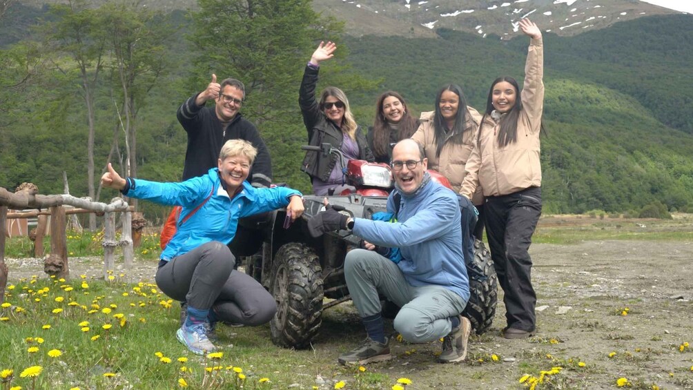 A group of people posing with a vehicle in a mountainous area with dandelions and trees. 1