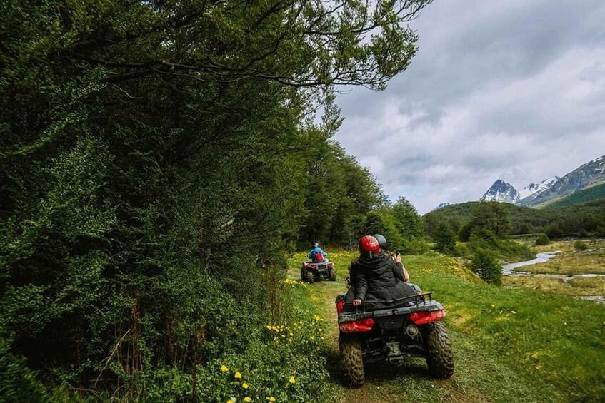 Two people riding ATVs on a narrow path surrounded by dense forest and mountains. 5