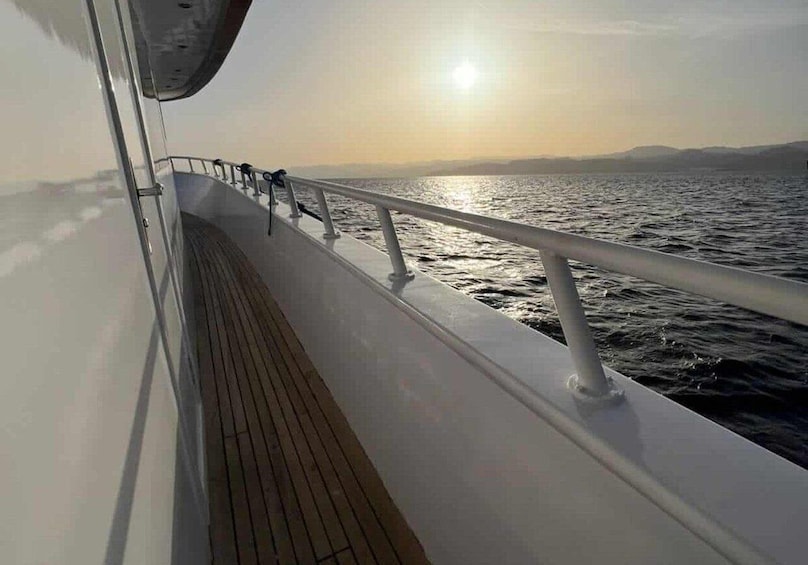 A ship's deck with a railing and a view of the ocean at sunset. 4