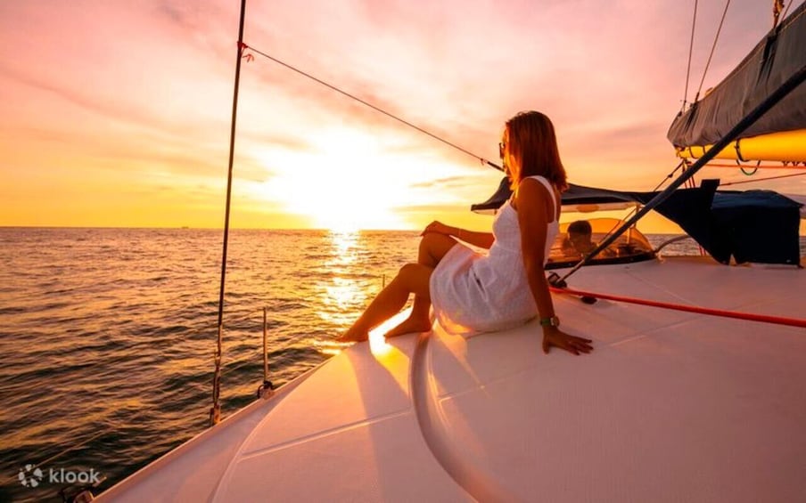 A woman sitting on a sailboat deck during sunset. 1