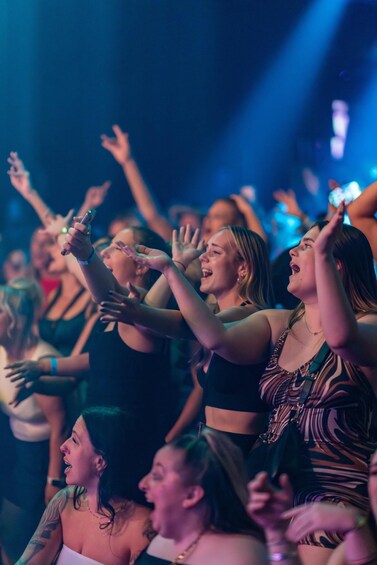 A crowd of people at a concert with raised hands and a stage in the background. 5