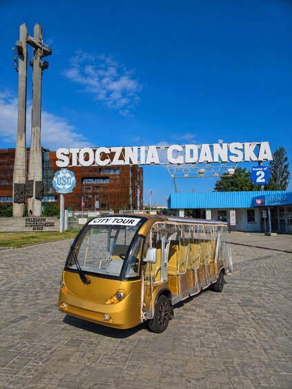A yellow city tour vehicle in front of a building with 'STOCZNIAC CADANSKA' signage. 1