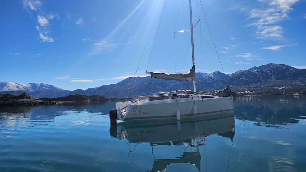 A sailboat named VAIU anchored in calm waters with a mountainous backdrop. 5