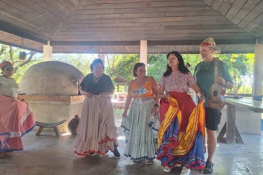 A group of people in traditional attire, a large stone oven, and a guitar player. 3
