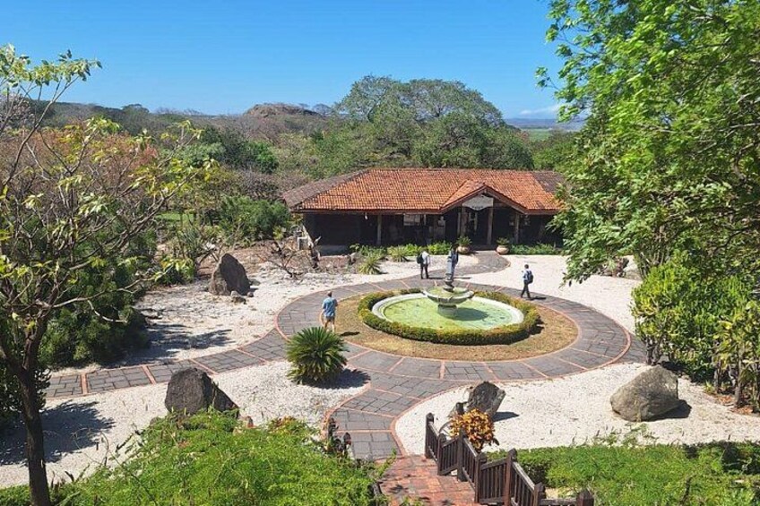 A landscaped garden with a central fountain, a building with a red-tiled roof, and surrounding greenery. 5