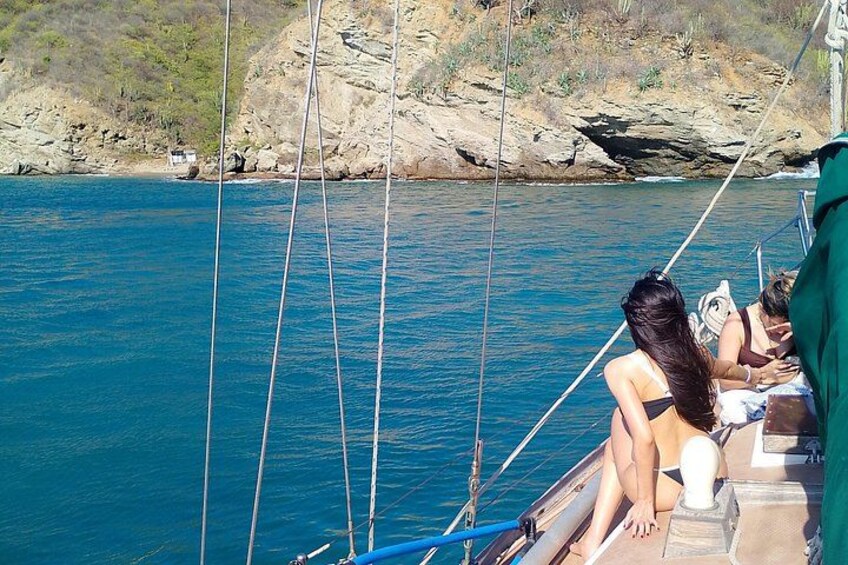 A sailboat with people on board, calm blue water, and rocky coastline. 4