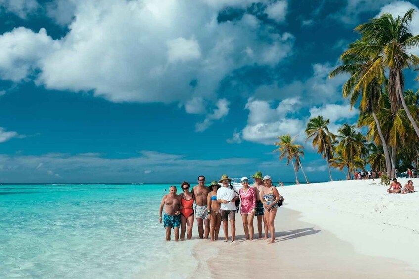 A group of people on a white sandy beach with clear turquoise water and palm trees under a blue sky with clouds. 1