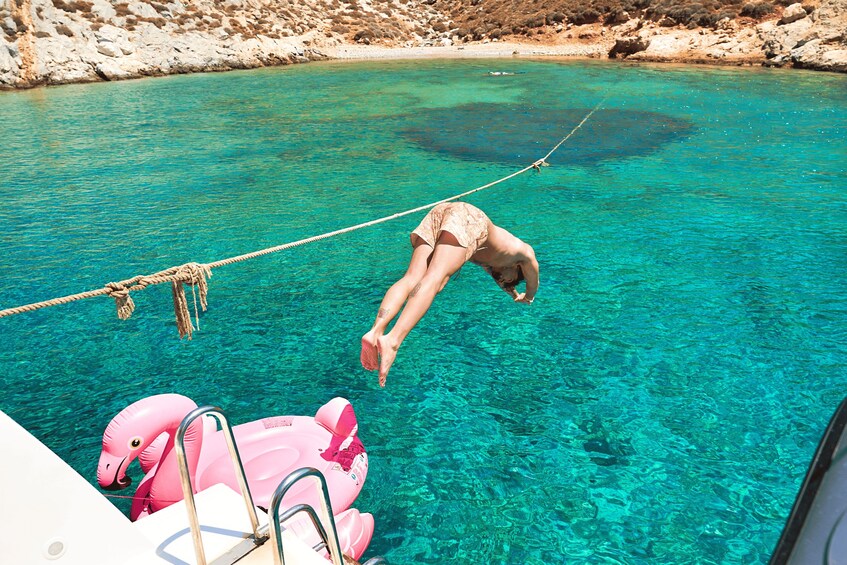 A person hanging from a rope over a body of water, with a boat and pink inflatable float nearby. 2