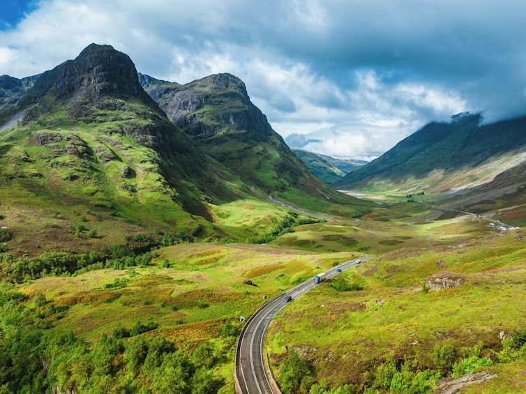 A winding road through a mountainous landscape with green hills and rocky peaks. 1