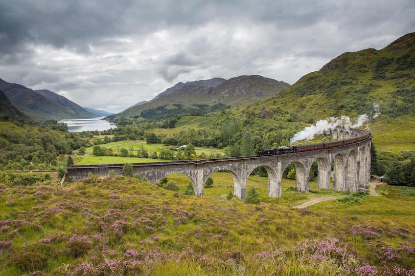 A train on a stone viaduct over a valley with a lake in the background. 3