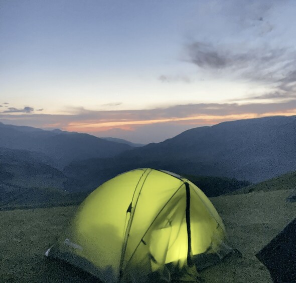 A yellow tent on a mountain with a sunset in the background. 2