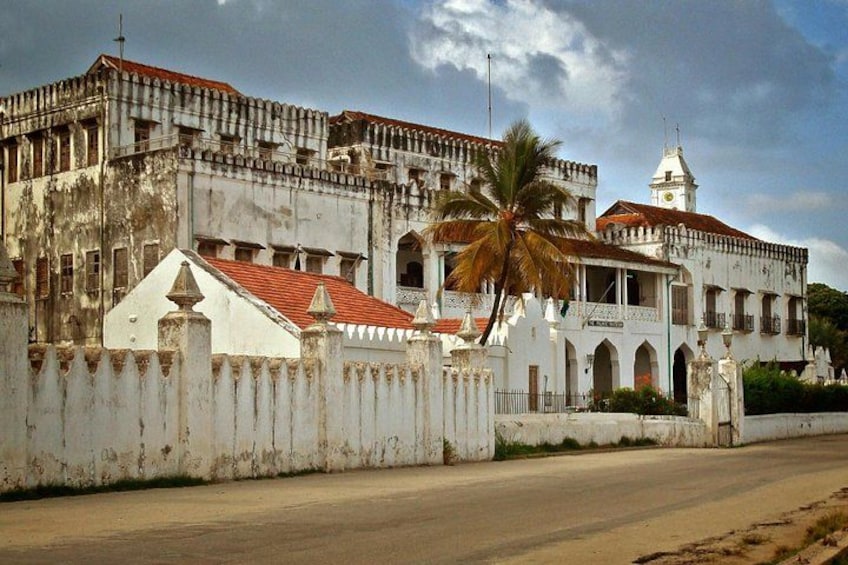 A historic building with a clock tower, palm trees, and a white fence. 5