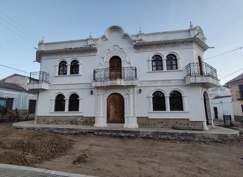 A white colonial-style house with a central entrance, two balconies, and decorative arches. 4