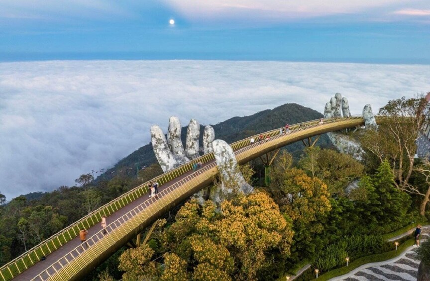 A suspension bridge with a unique rock hand design, surrounded by lush greenery and a view of the sea below. 1