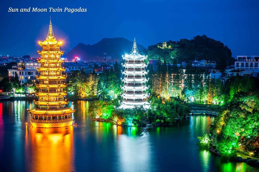 Two illuminated pagodas by a calm river with surrounding greenery and a mountain backdrop. 1