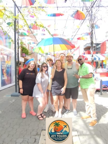 A group of people posing for a photo on a sunny street with colorful umbrellas overhead. 5