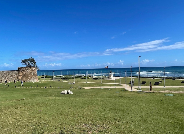 A coastal park with a grassy area, a stone wall, a flag, and the ocean in the background. 2