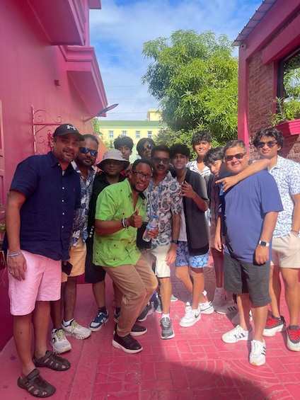 A group of people standing in a narrow alley with pink walls and a brick building in the background. 1