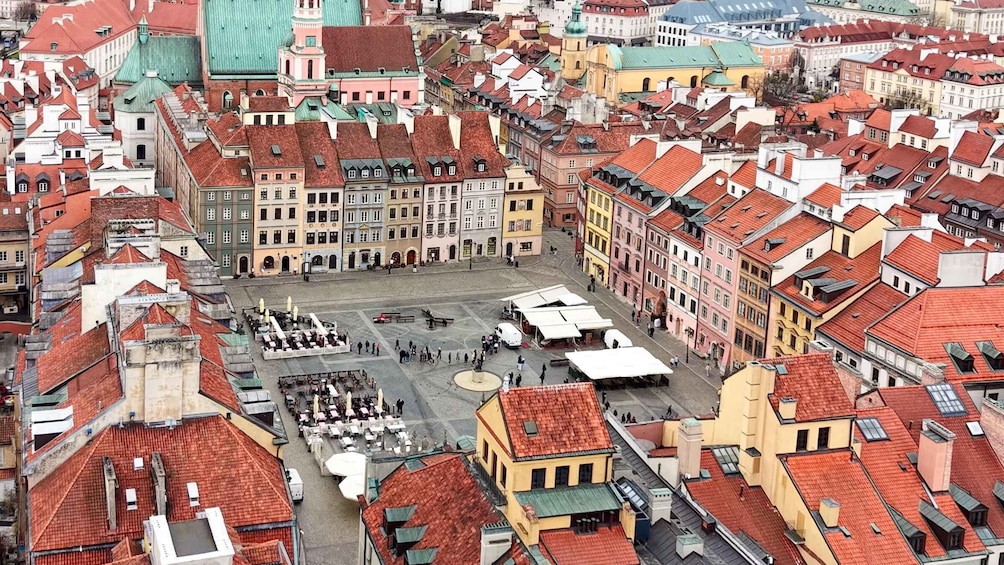Una piazza storica europea con edifici dai tetti rossi, uno spazio aperto centrale e zone con tavoli all'aperto. 1