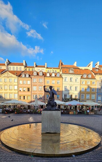 Ein Platz mit einer zentralen Statue, Kopfsteinpflaster und bunten Gebäuden im Hintergrund. 1
