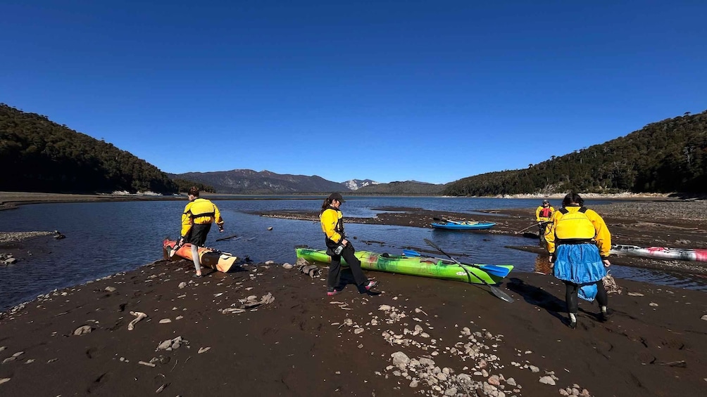 Three people on a beach with kayaks and a canoe, surrounded by water and mountains. 1