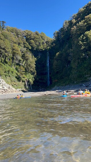 A river with kayaks, a waterfall, and dense forest. 3