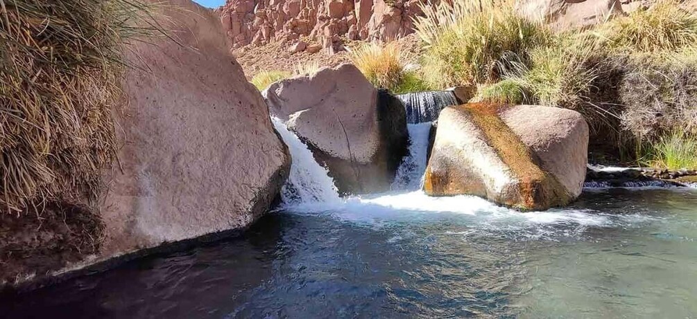 A small waterfall flowing over rocks in a dry riverbed with sparse vegetation. 1