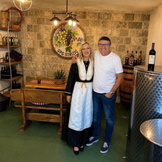 A man and a woman standing in a wine cellar with wooden shelves and a barrel labeled 'OPG STRIZIC.' 3