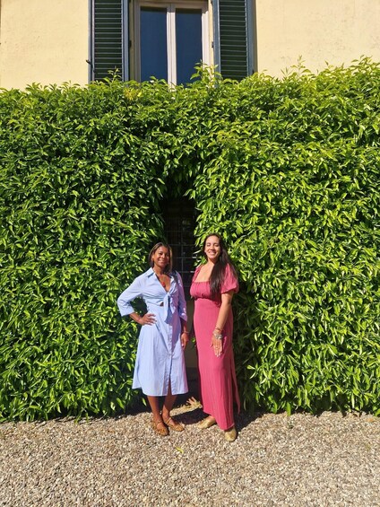 Two people standing in front of a hedge with a building in the background. 5
