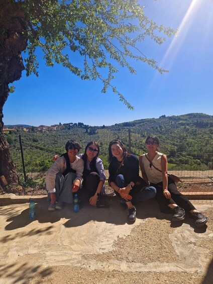 Four people sitting on a ledge with a view of a hilly landscape and a distant castle. 3